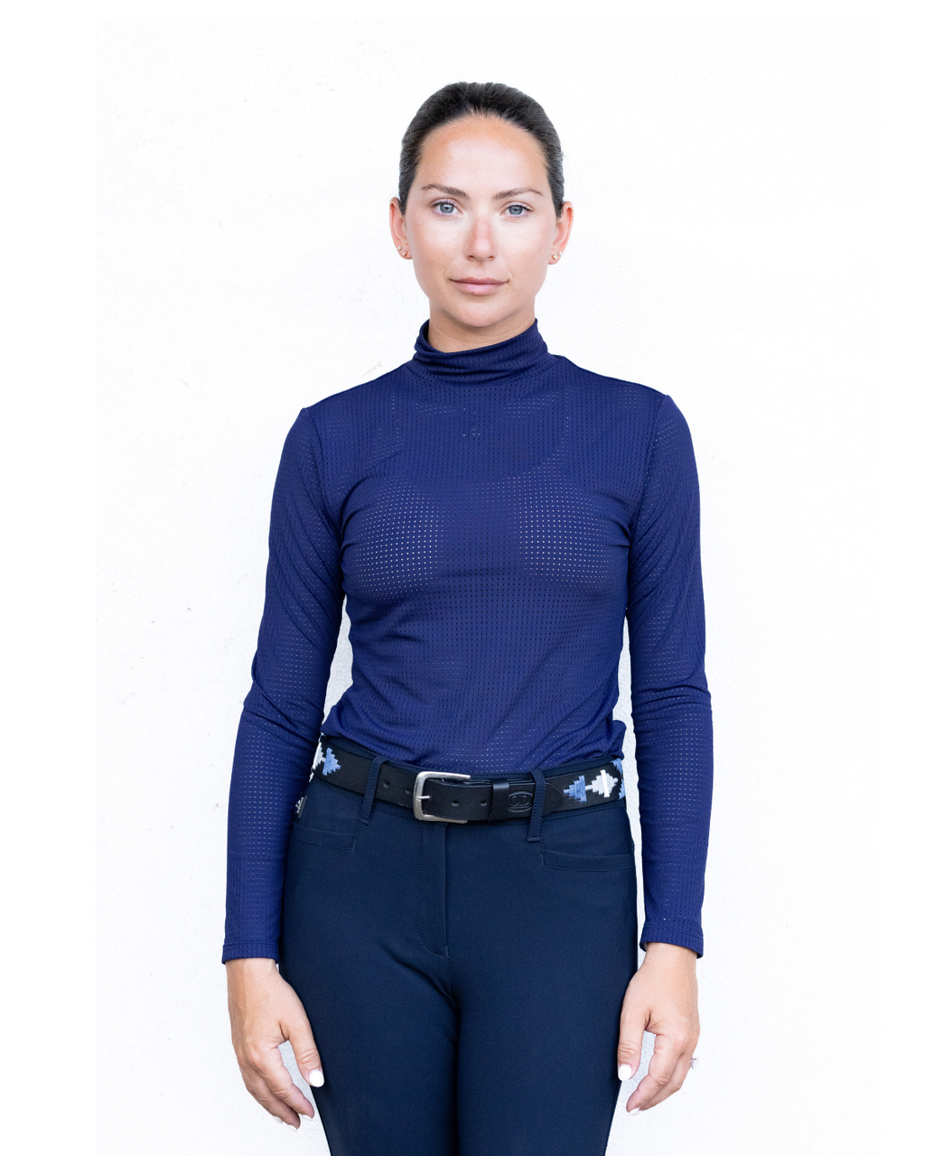 Woman wearing a blue long-sleeve top and navy riding pants on a white background