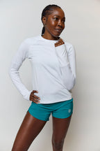 Woman wearing a white long-sleeve top and teal shorts on a plain background