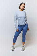 Woman wearing a light blue long-sleeve top and blue leggings on a white background