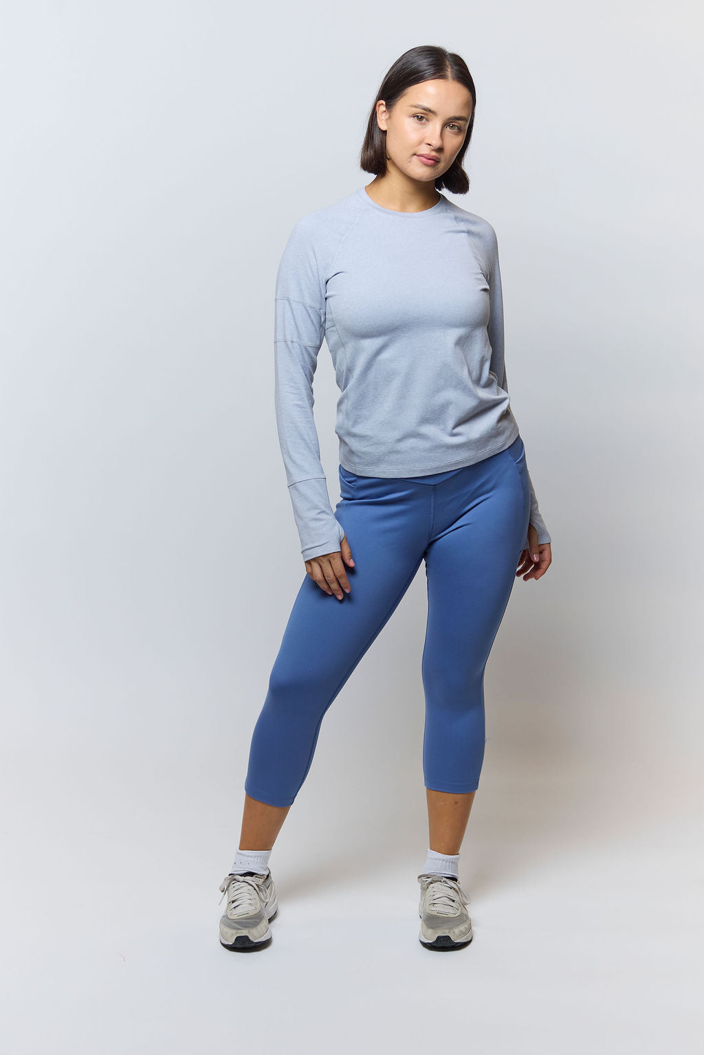 Woman wearing a light blue long-sleeve top and blue leggings on a white background