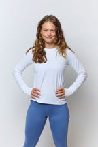 Woman wearing a white long-sleeve top and blue leggings on a light gray background