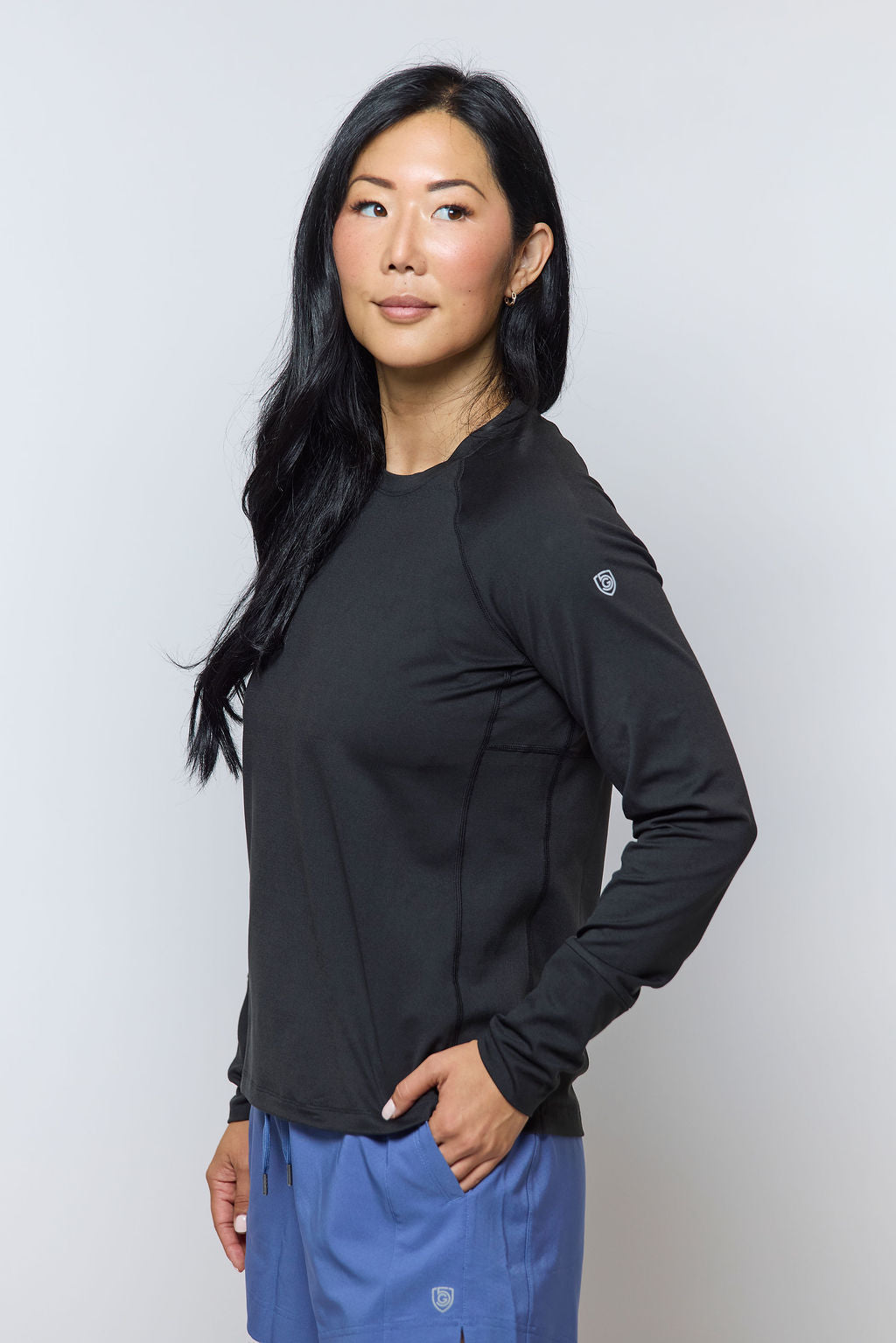 Woman wearing a black long-sleeve top and blue pants against a white background