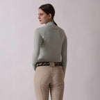 Woman wearing a light green equestrian jacket and beige pants on a plain background