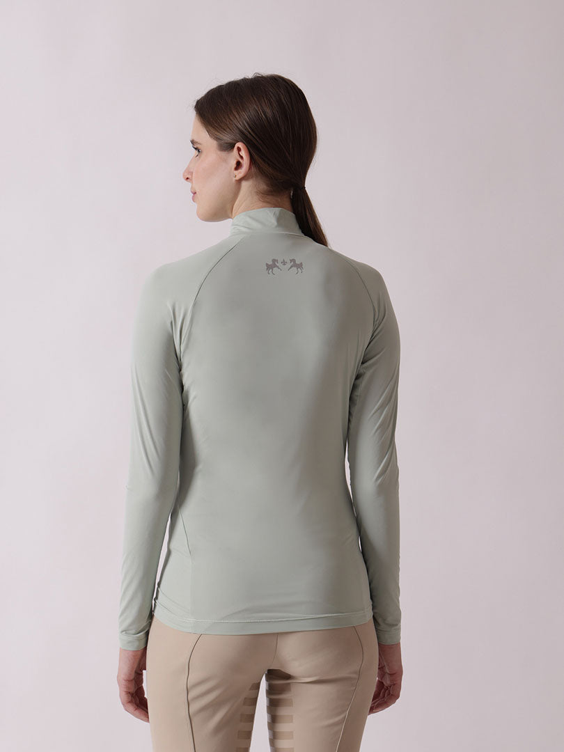 Woman wearing a light green long-sleeve top with a logo on the back against a light pink background