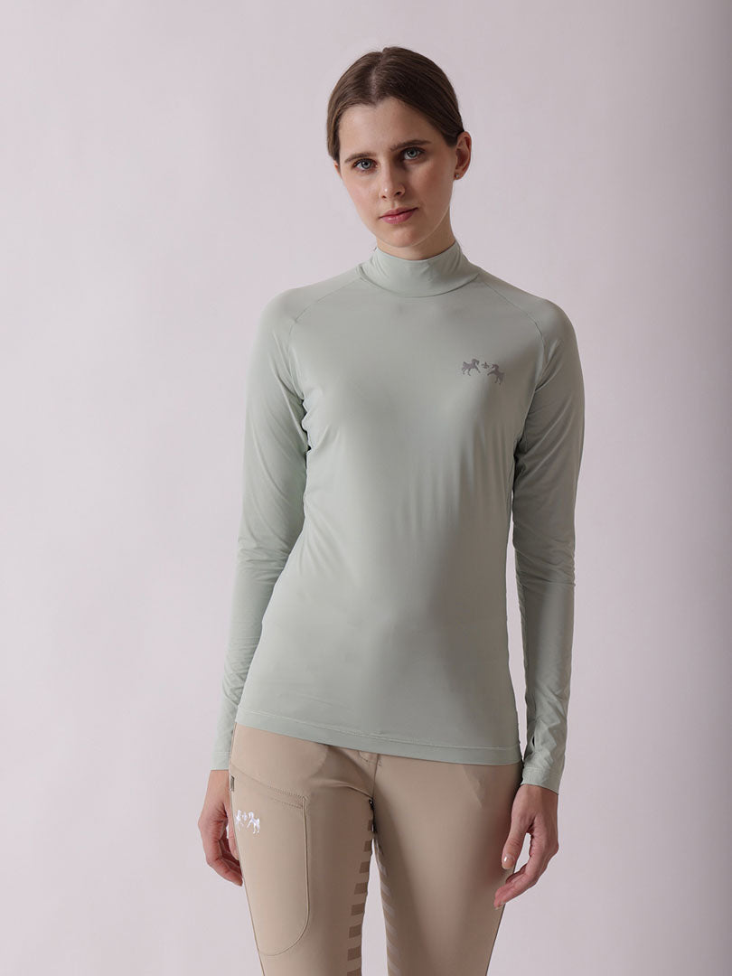 Woman wearing a light green long-sleeve top with a logo on a plain background