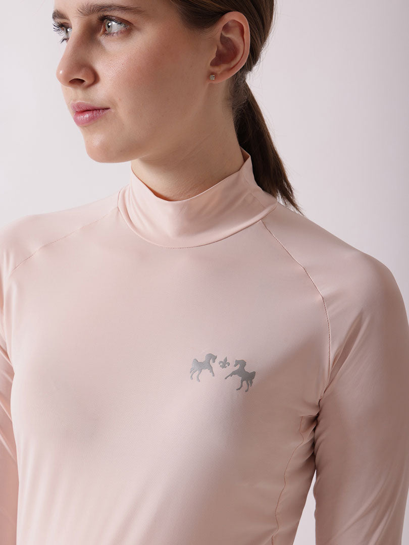 Woman wearing a light pink long-sleeve top with a logo on a plain background