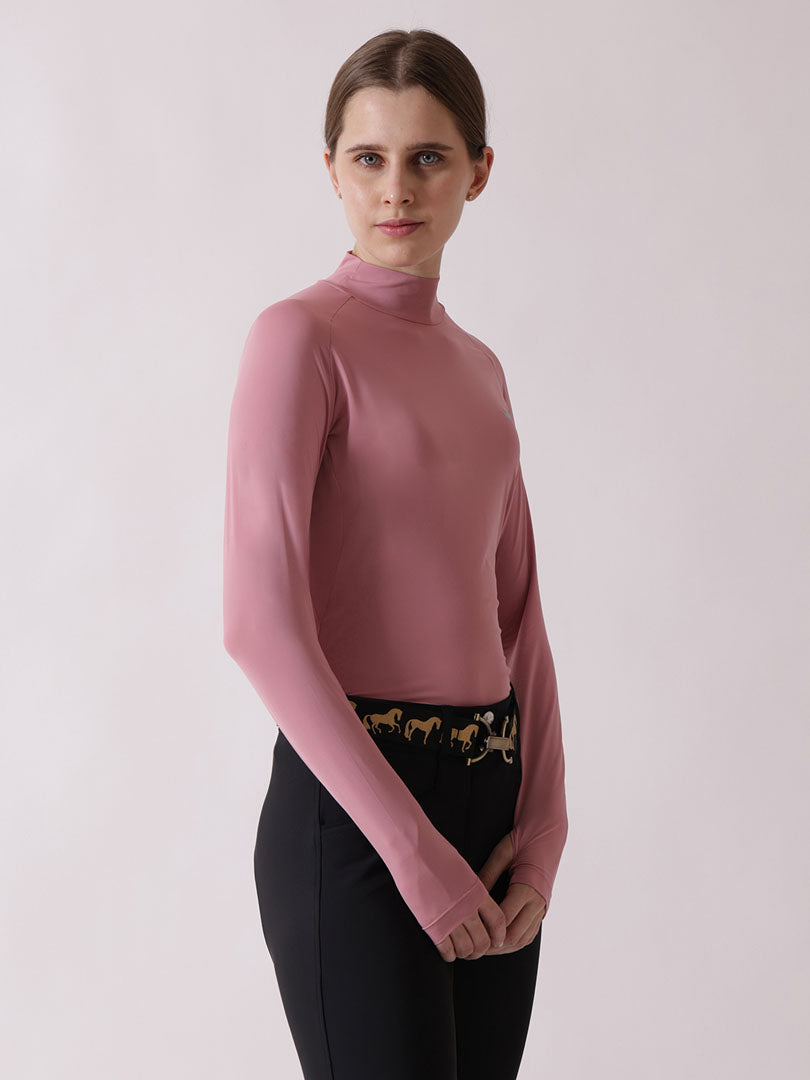 Woman wearing a pink turtleneck sweater and black pants with gold accents on a light gray background