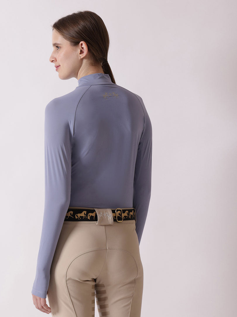 Person wearing a light blue long-sleeve top and beige riding pants on a white background