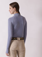 Person wearing a light blue long-sleeve top and beige riding pants on a white background