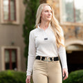 Woman in equestrian attire standing outdoors with a blurred background