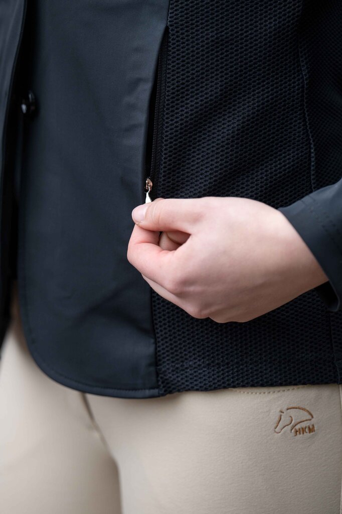 Person opening a black jacket with a mesh inner lining, wearing beige pants with a logo.