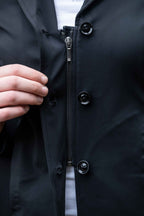 Close-up of a black jacket with buttons and a zipper, with a hand adjusting the zipper.