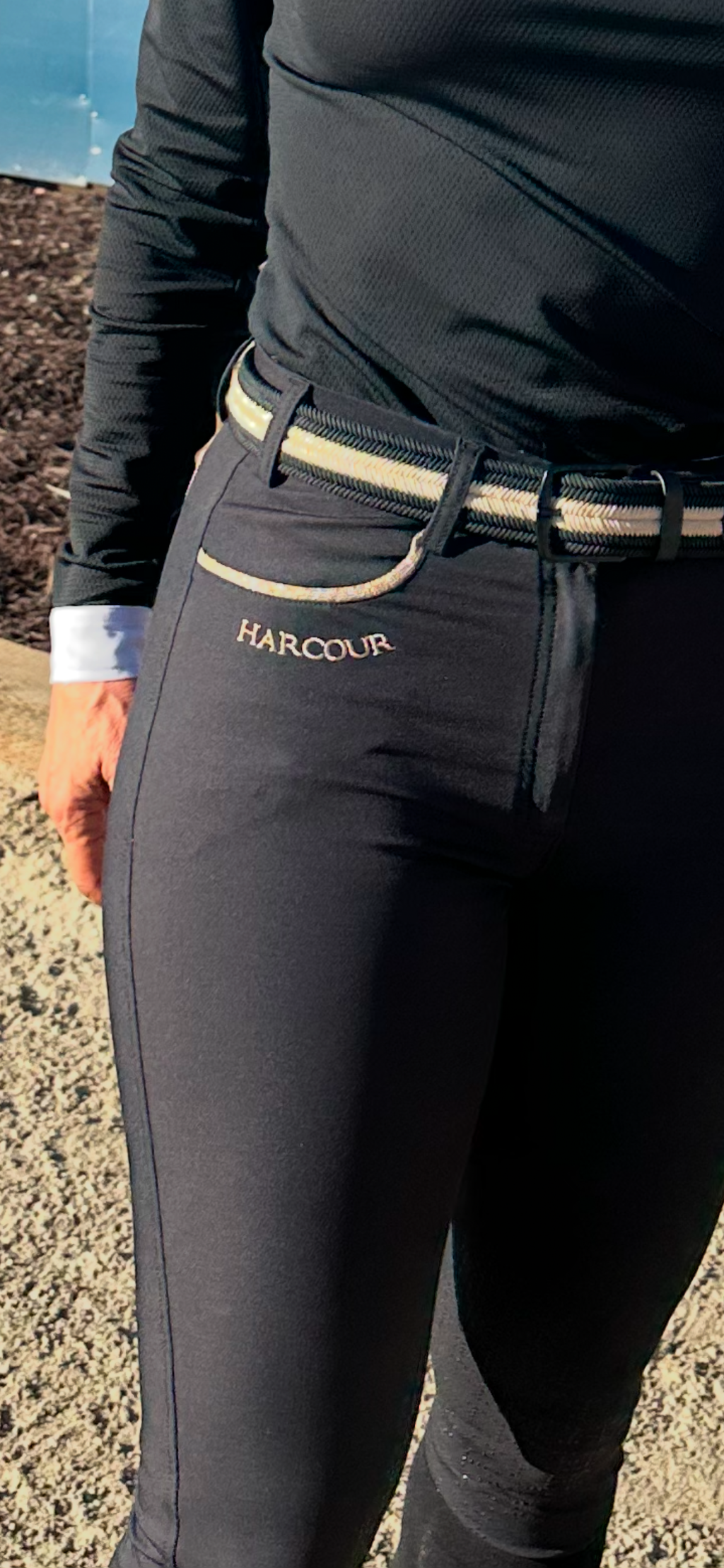 Person wearing black equestrian pants with a visible brand logo, standing on a gravel surface.