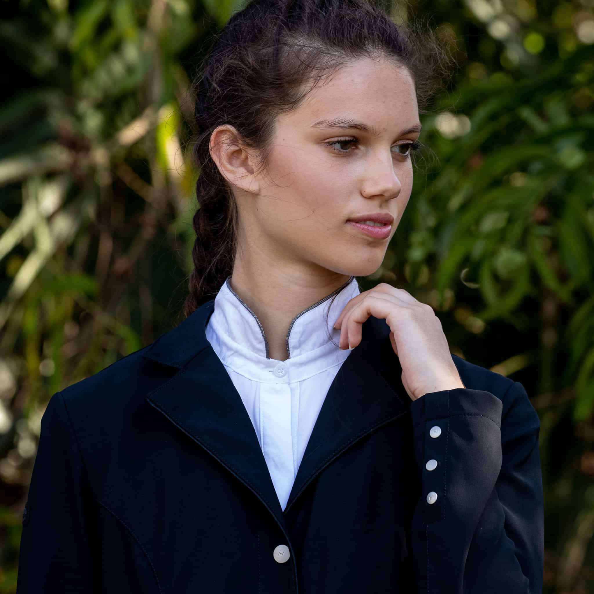 Woman wearing a dark airbag-compatible equestrian coat with white buttons against a blurred green background