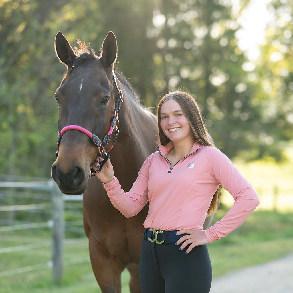 Woman in a pink shirt standing next to a horse in an outdoor setting