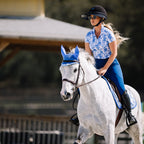 Woman riding a white horse wearing a blue bridle in an outdoor setting