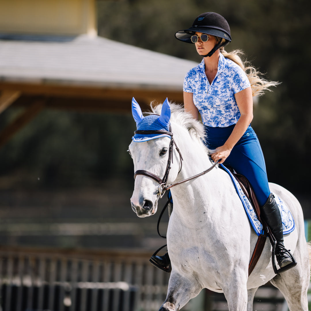 Woman riding a white horse wearing a blue bridle in an outdoor setting