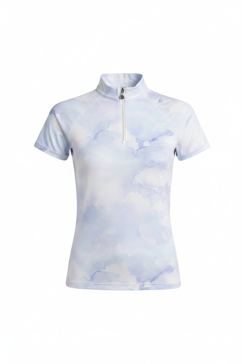 Woman wearing a light blue equestrian shirt with cloud pattern and purple riding pants on a gray background