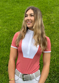 Woman wearing a pink and white equestrian outfit standing on grass