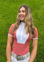 Woman wearing a pink and white equestrian outfit standing on grass