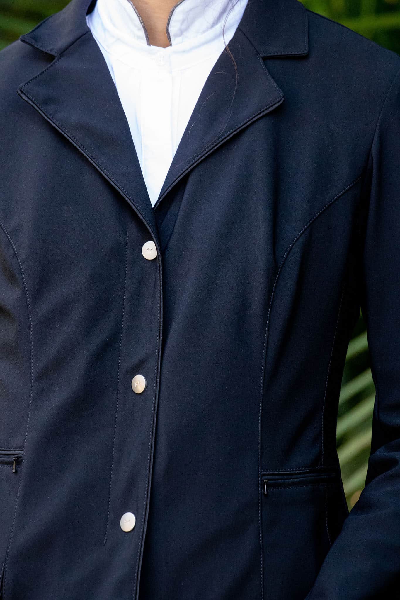 Navy blue airbag-comptabile equestrian show coat with white shirt underneath, blurred green background