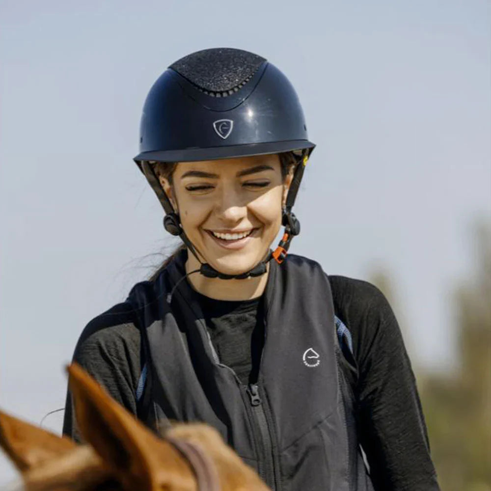 Person wearing a helmet and riding jacket, standing next to a horse with a blurred background