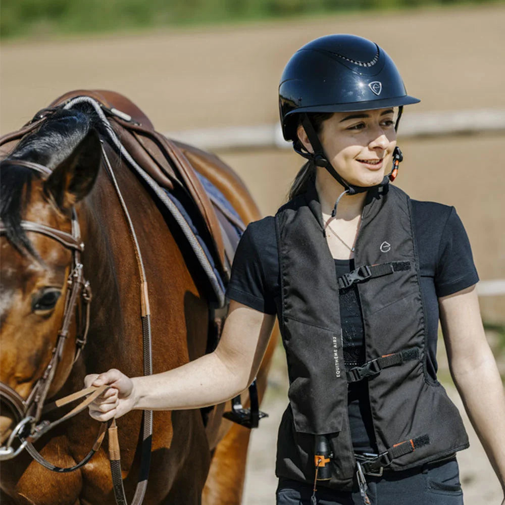 Woman in equestrian gear standing next to a horse on a track