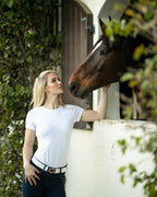 Woman in a white shirt and black pants standing next to a horse, both looking at each other.