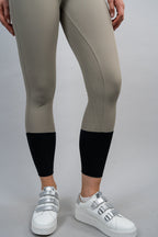 Beige riding leggings with black cuffs worn by a person on a gray background