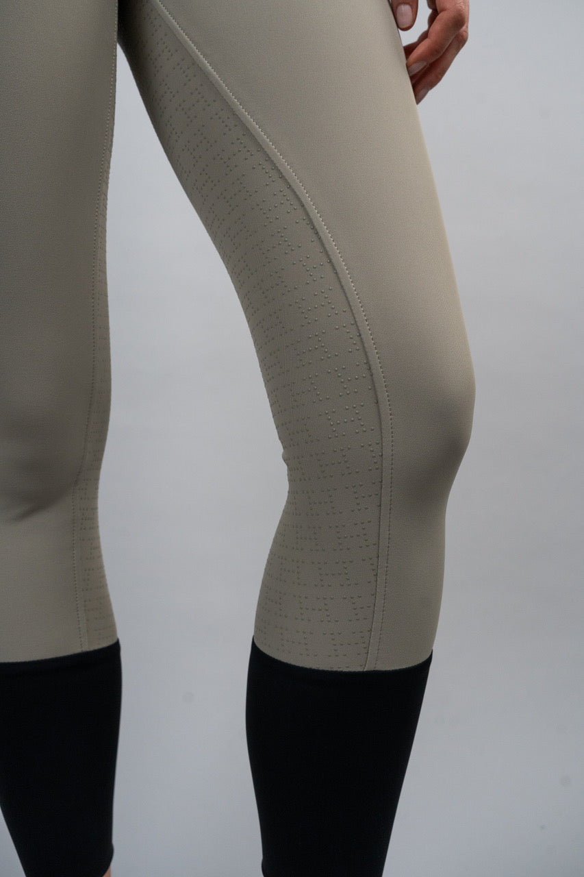 Close-up of beige riding pants with black boots on a plain background