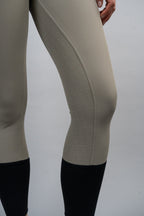 Close-up of beige riding pants with black boots on a plain background