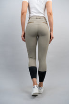 Person wearing beige riding pants with black leg warmers on a gray background