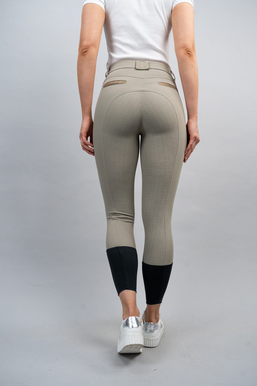 Person wearing beige riding pants with black leg warmers on a gray background