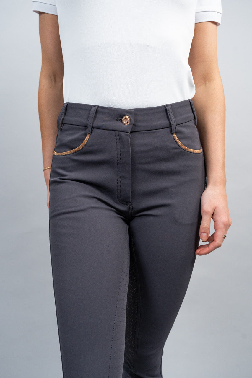 Person wearing dark gray riding pants with a white top on a light gray background