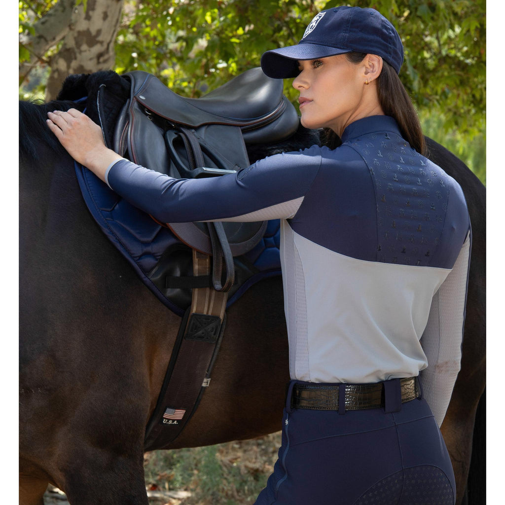 Woman in equestrian attire adjusting a saddle on a horse outdoors.