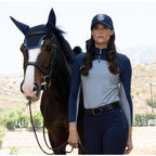 Woman in equestrian attire standing next to a horse with a scenic background