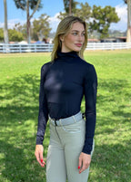 Woman wearing a navy long-sleeve top and light gray riding pants in an outdoor setting.