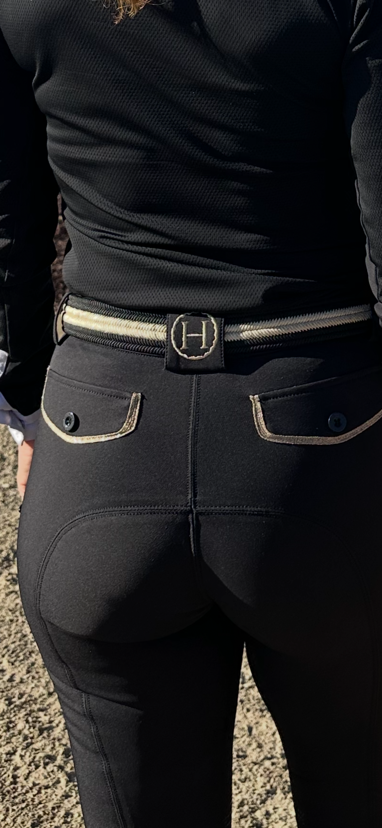 Person wearing black riding pants with a silver belt buckle on a textured ground.