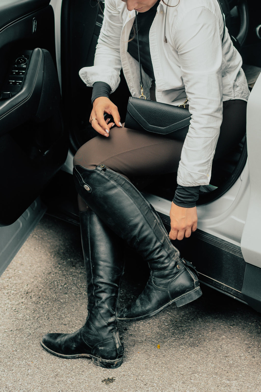 Person sitting in a car wearing black knee-high boots and a white jacket.