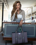 Woman holding a gray tote bag with a green emblem in an indoor setting