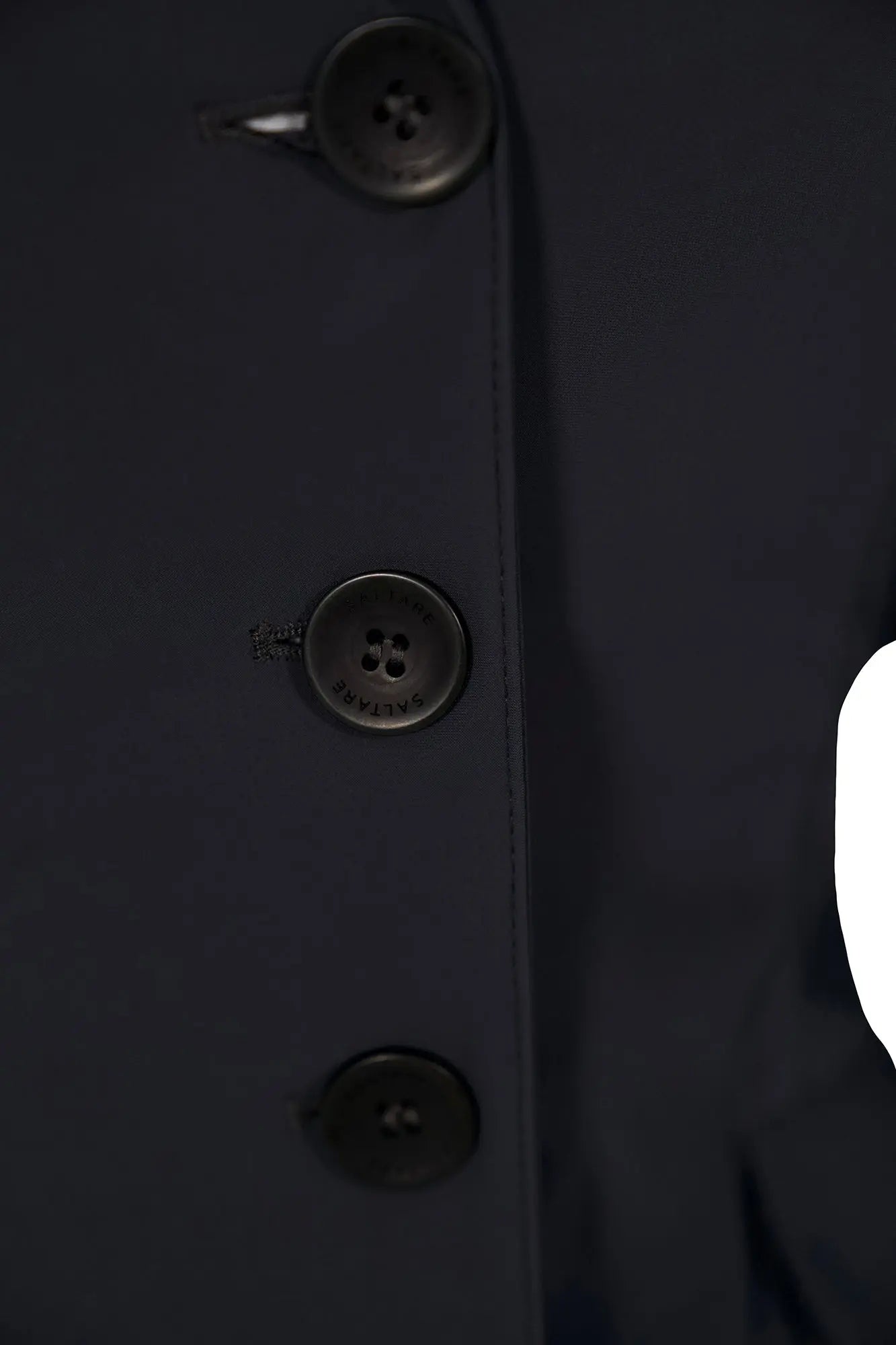 Close-up of a dark coat with button details on a plain background