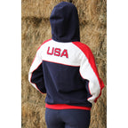 Person wearing a hoodie with 'USA' on the back, standing in front of hay bales.