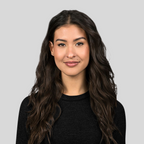 Woman with long dark hair wearing a black top against a light gray background