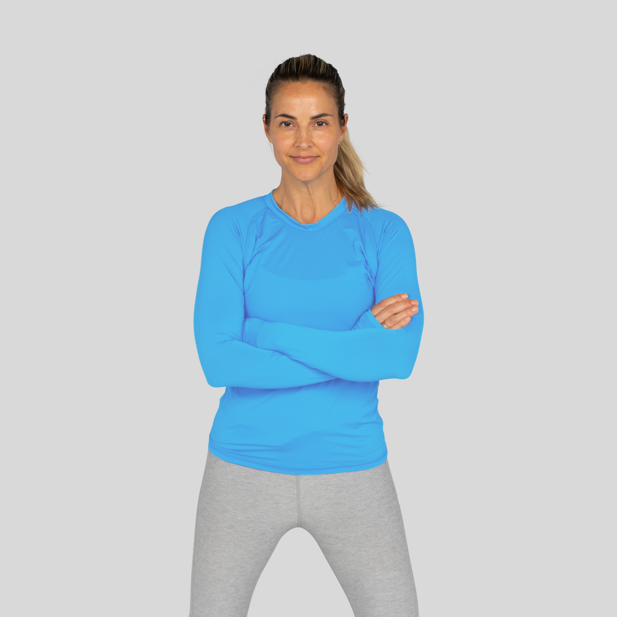 Woman wearing a blue long-sleeve top and gray leggings on a light gray background