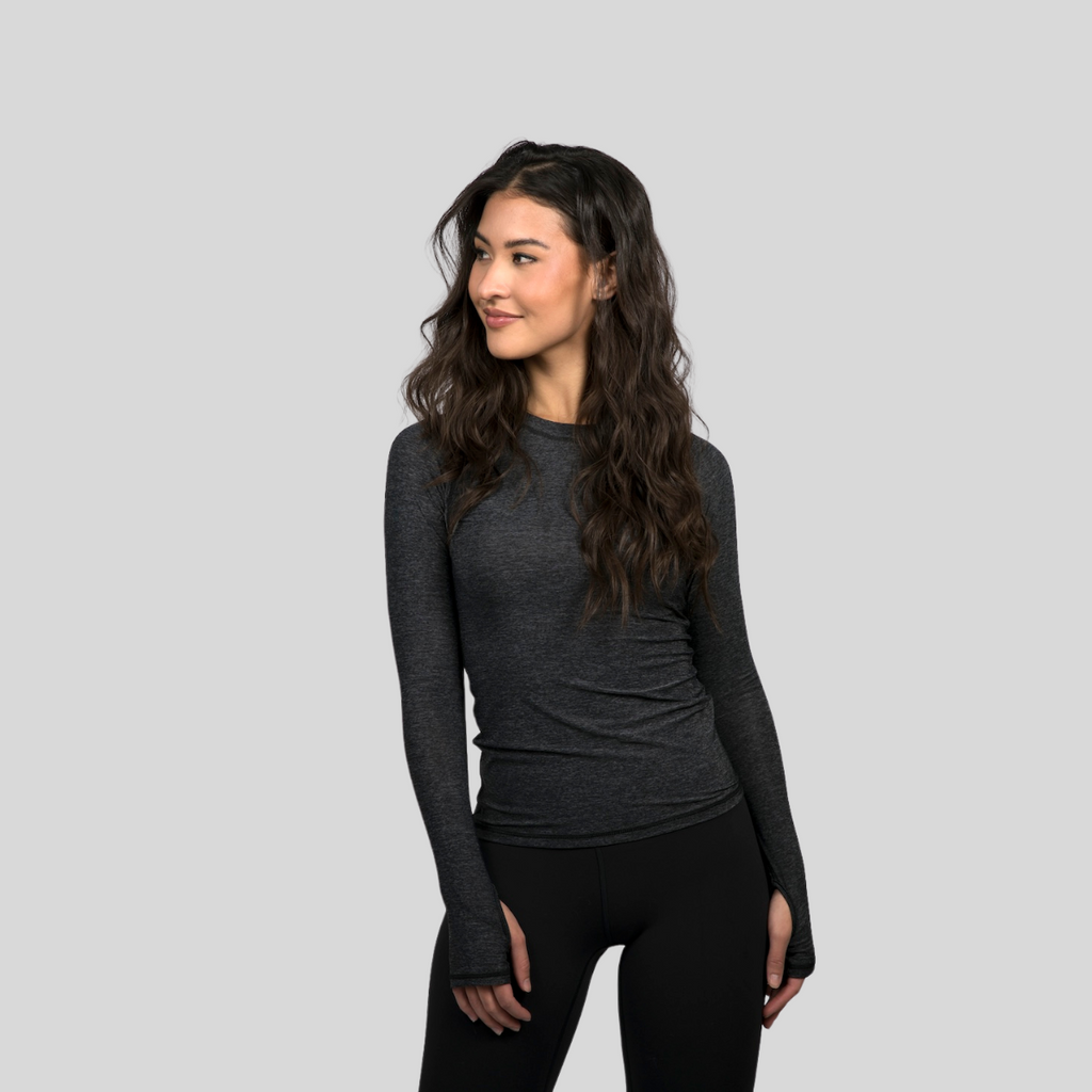 Woman wearing a dark gray long-sleeve top and black leggings on a light gray background