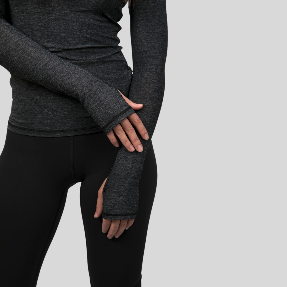 Person wearing dark gray long-sleeve top and leggings on a light gray background