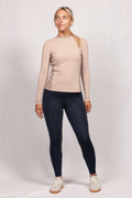 Woman wearing a beige long-sleeve top and black leggings on a white background