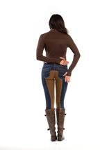 Person wearing a brown turtleneck, blue jeans, and brown boots on a white background