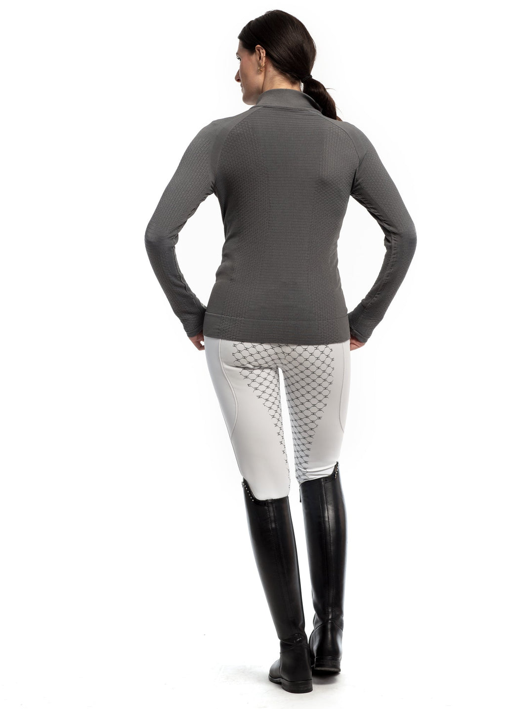 Person wearing a gray long-sleeve top and white pants with black riding boots on a white background