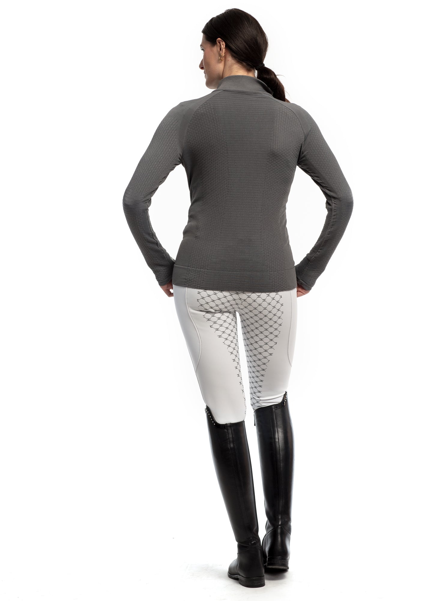 Person wearing a gray long-sleeve top and white pants with black riding boots on a white background